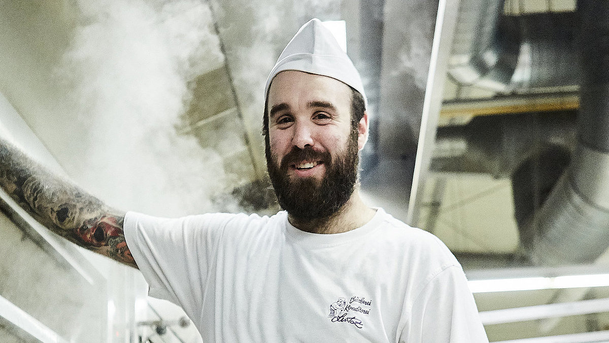 Bäcker steht vorm Ofen und lächelt in die Kamera