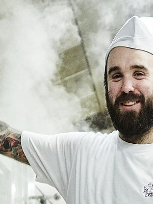 Bäcker steht vorm Ofen und lächelt in die Kamera