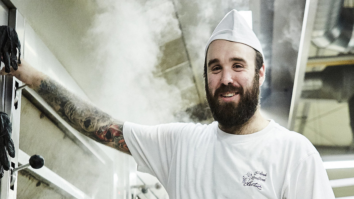 Bäcker steht vorm Ofen und lächelt in die Kamera