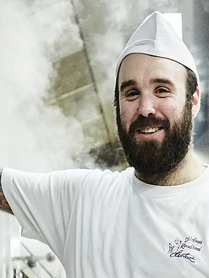 Bäcker steht vorm Ofen und lächelt in die Kamera