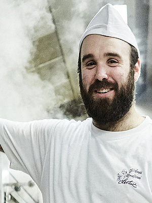 Bäcker steht vorm Ofen und lächelt in die Kamera