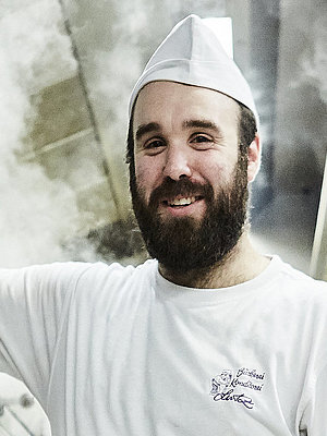 Bäcker steht vorm Ofen und lächelt in die Kamera