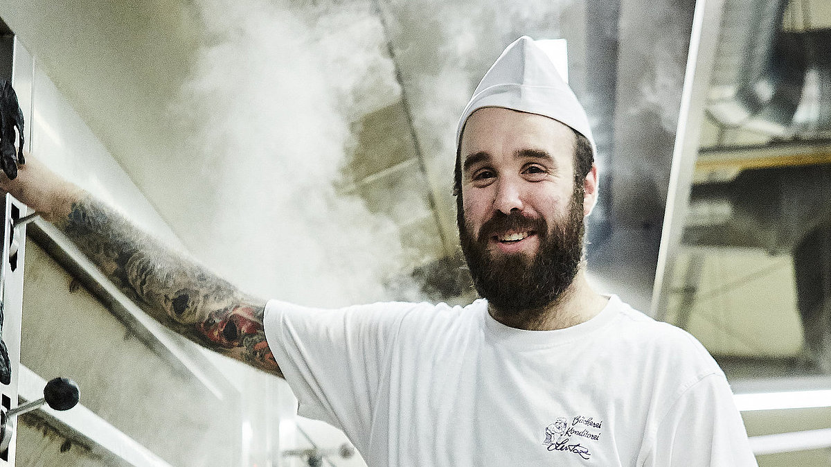 Bäcker steht vorm Ofen und lächelt in die Kamera