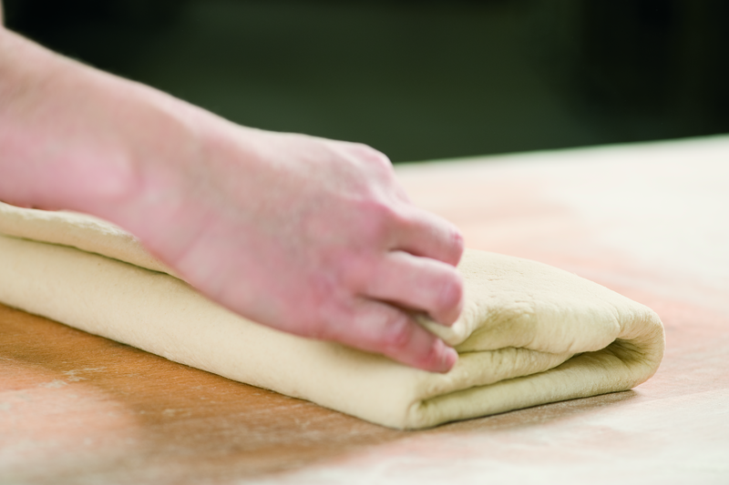 Bäcker legt ausgerollten Teig zusammen