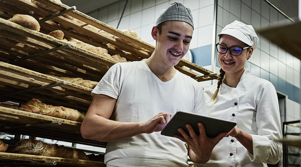 Zwei Bäcker besprechen etwas und schauen auf ein Klemmbrett