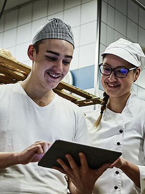 Zwei Bäcker besprechen etwas und schauen auf ein Klemmbrett