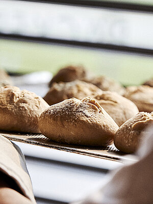 Blick über die linke Schulter eines Bäckers, der gerade Brötchen in eine Ablage schiebt