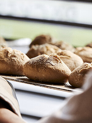 Blick über die linke Schulter eines Bäckers, der gerade Brötchen in eine Ablage schiebt