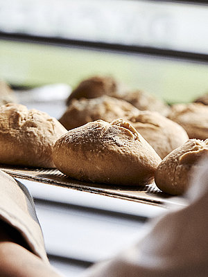 Blick über die linke Schulter eines Bäckers, der gerade Brötchen in eine Ablage schiebt
