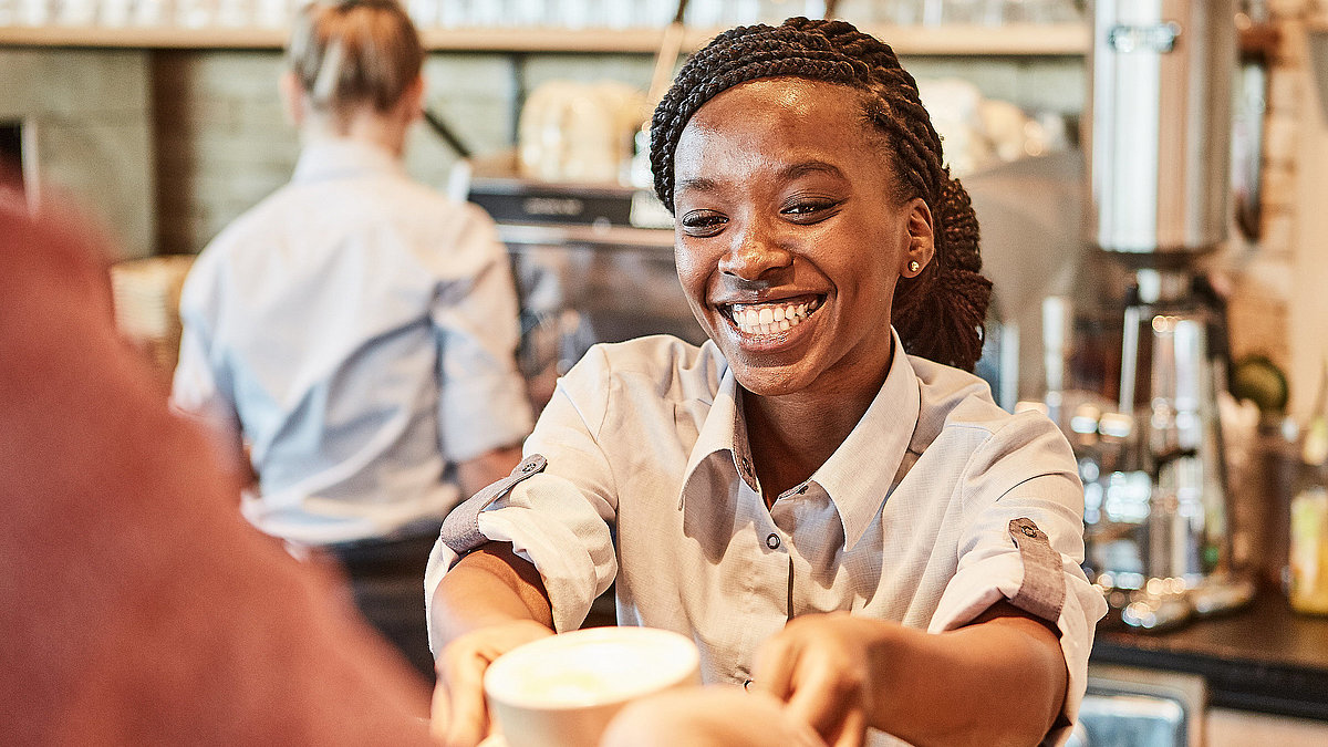 Bäckereifachverkäuferin stellt einen Kaffee auf den Thresen