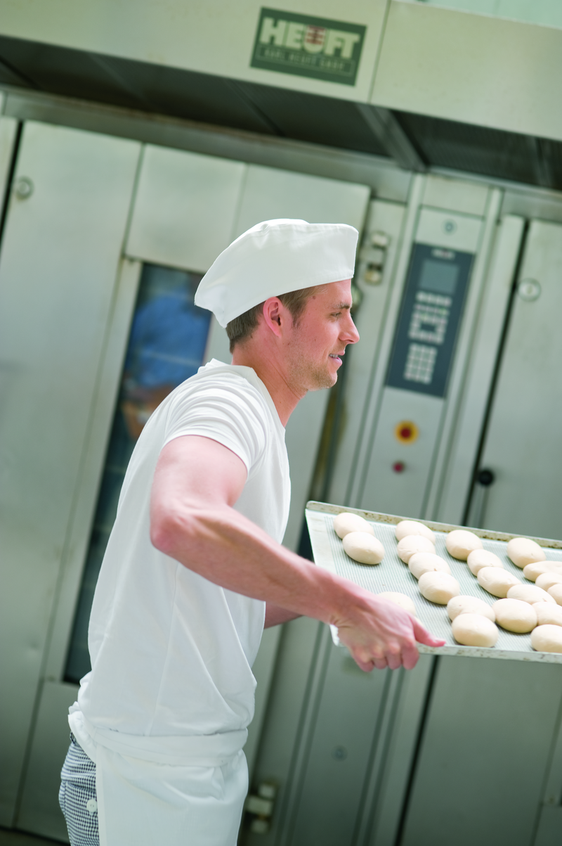 Bäckergeselle trägt ein Backblech mit Brötchenteiglingen