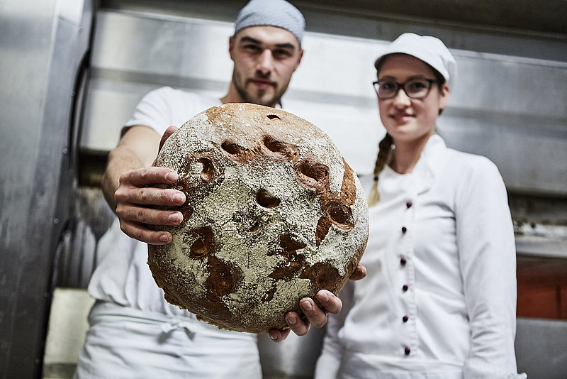 Bäcker und Bäckerazubine halten stolz Brot