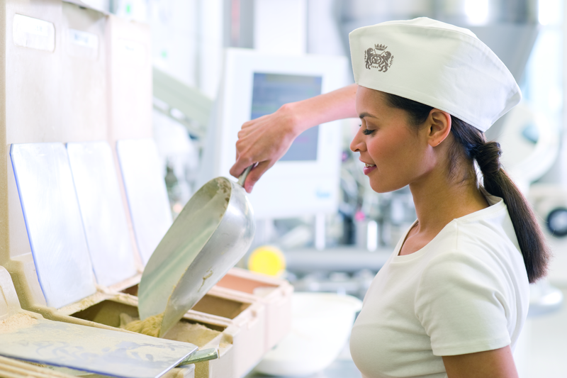 Bäckergesellin mischt Zutaten mit Abwiegschaufel