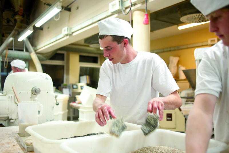 Bäckergesellen wälzen Brötchenteig in Mohn