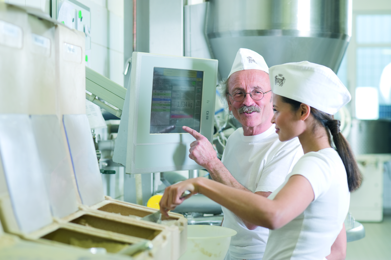 Bäckermeister und Bäckergesellin mischen einen Teig am Rezeptcomputer