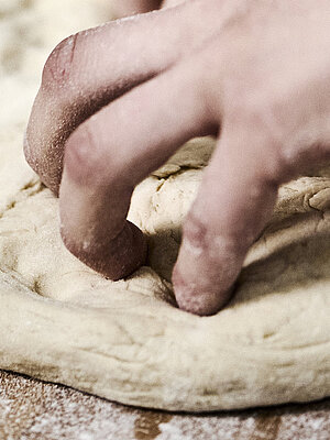 Bäckerhände bearbeiten einen flach ausgebreiteten Teig auf einer mehligen Arbeitsfläche. 