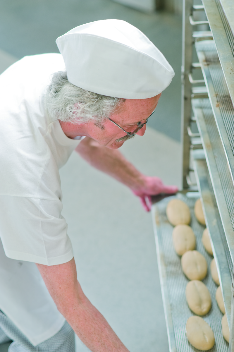Bäckermeister schiebt ein Backblech mit Brötchenteiglingen in einen Stikken