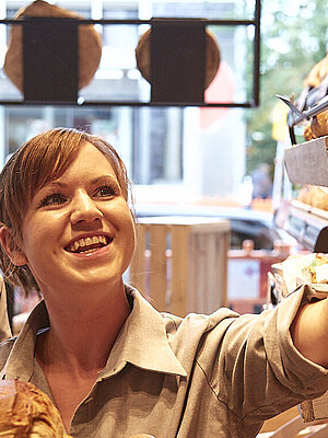 Bäckereifachverkäuferin nimmt Brot aus der Auslage