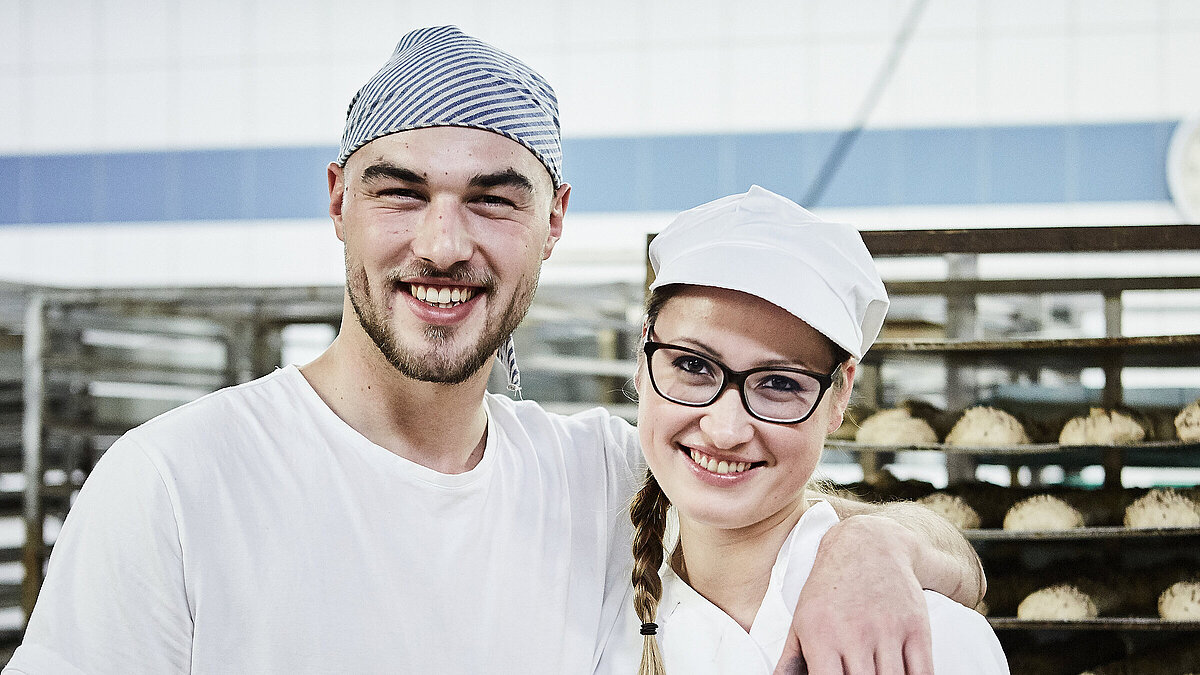 Zwei Bäcker, im Hintergrund ein Rollwagen mit Gebäck