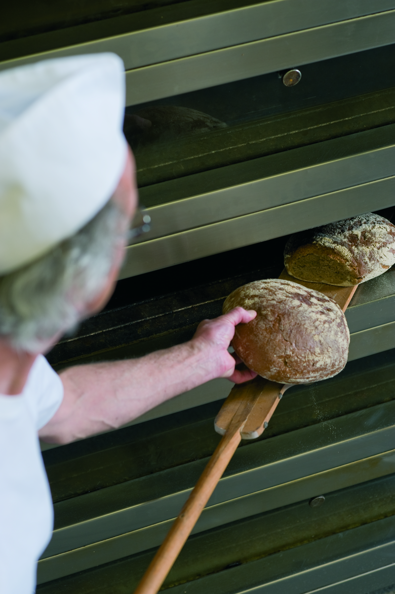 Bäckermeister überprüft auf einem Schießer Brote aus dem Etagenofen