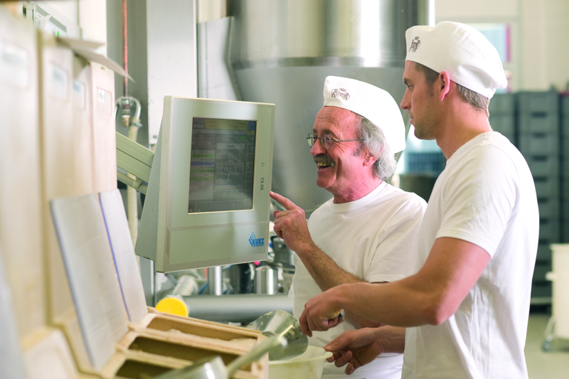 Bäckermeister und Bäckergeselle mischen einen Teig am Rezeptcomputer