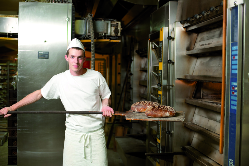 Bäckergeselle mit 2 Broten auf Schießer vor Ofen