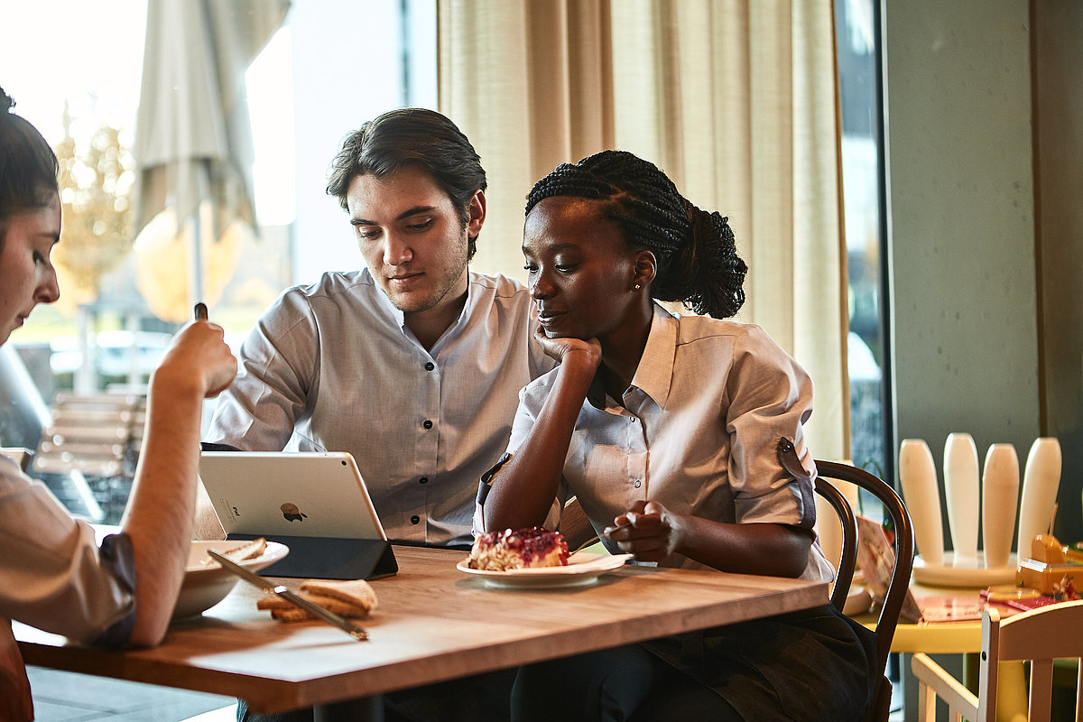 Zwei Personen sitzen an einem Tisch und schauen in ein Tablet
