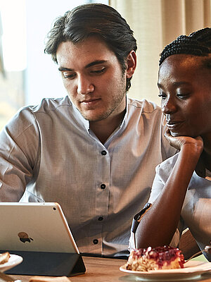 Zwei Personen sitzen an einem Tisch und schauen in ein Tablet