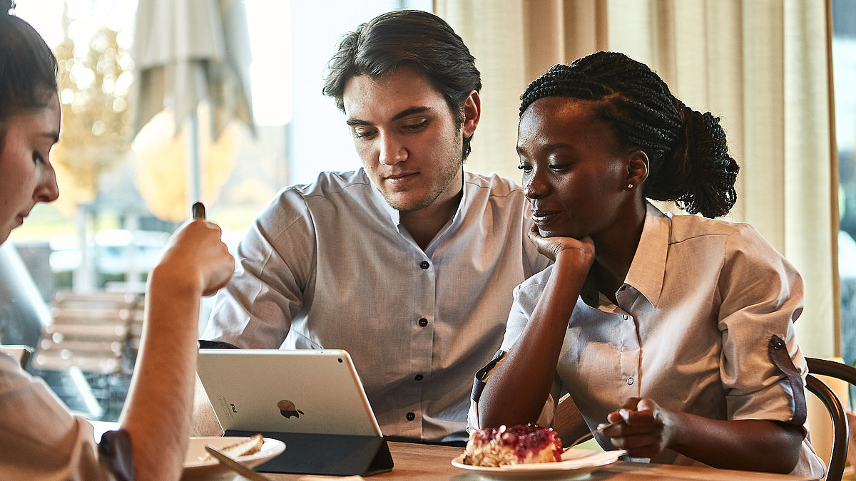 Zwei Personen sitzen an einem Tisch und schauen in ein Tablet