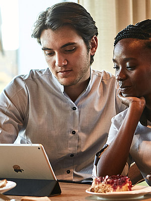 Zwei Personen sitzen an einem Tisch und schauen in ein Tablet