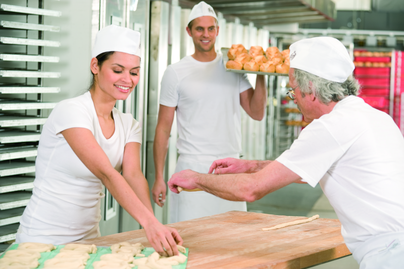 Bäckermeister und Bäckergesellin formen Teig zu Brezeln