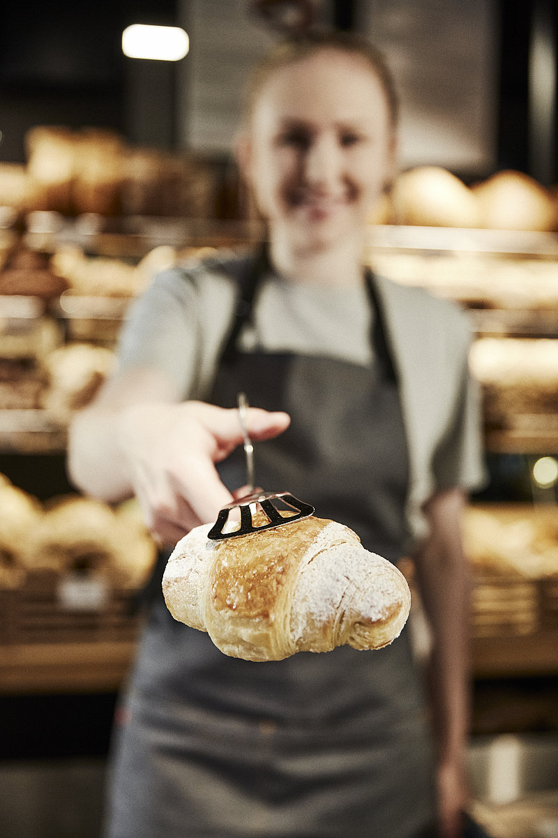 Verkäuferin reicht Croissant mit Zange
