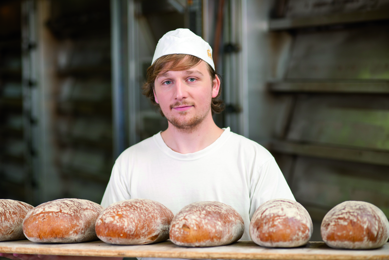 Auszubildender mit frisch gebackenen Broten auf Holzbrett