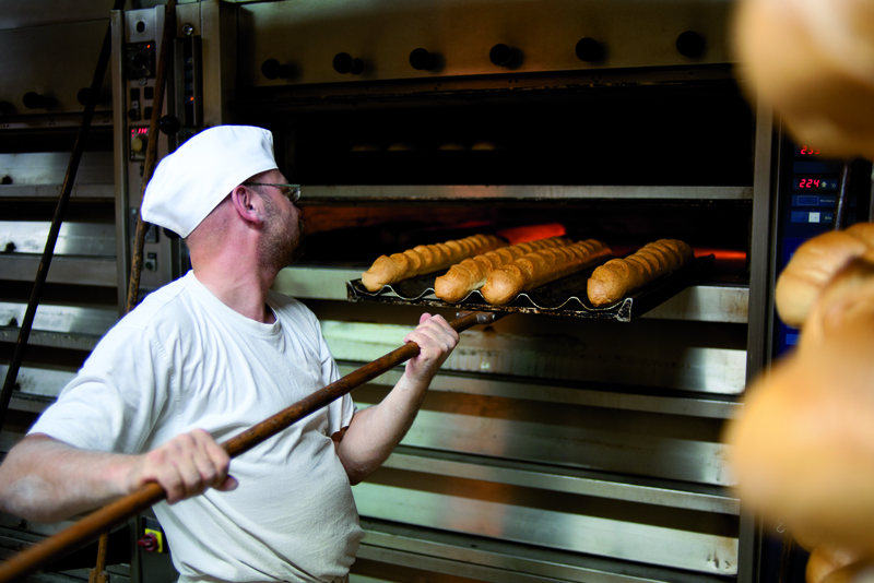 Bäcker holt Baguettes mit Schießer aus dem Ofen