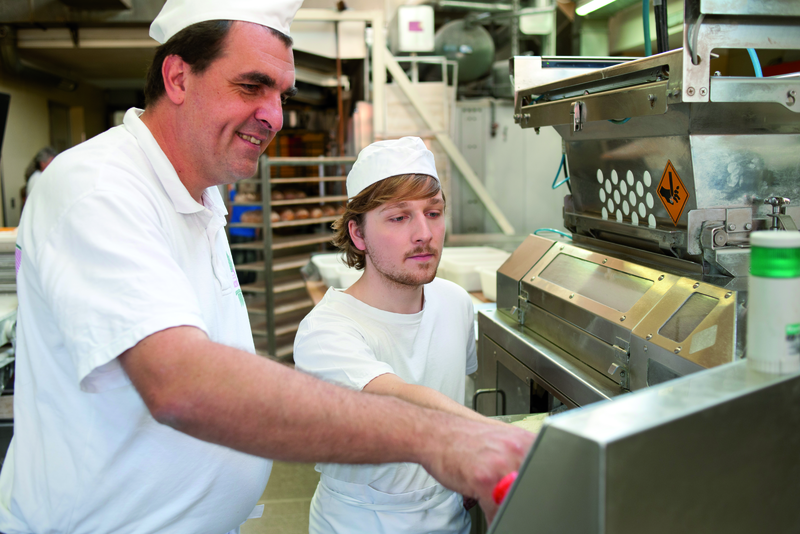 Bäckermeister erklärt Azubi Maschine in der Backstube