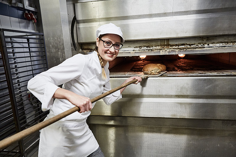 Bäcker Azubine holt Brote aus dem Ofen