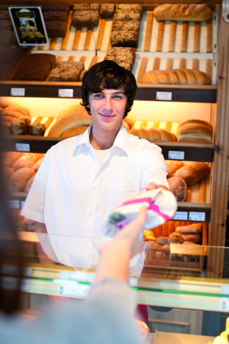 Auszubildender reicht Ware über die Theke