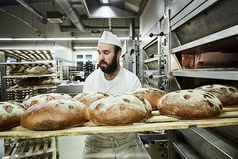 Bäckermeister holt Brote aus dem Ofen