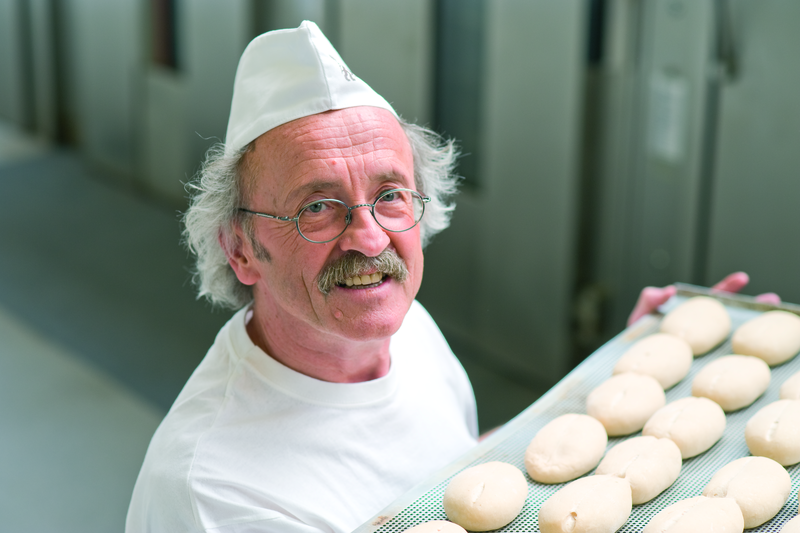Bäckermeister trägt ein Backblech mit Brötchenteiglingen