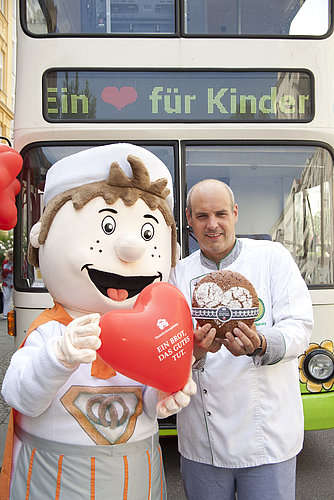 Bäckman mit einem Luftballon-Herz und ein Bäcker mit einem Brot posieren vor der Kamera