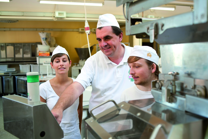 Bäckermeister erklärt Azubis Maschine in der Backstube