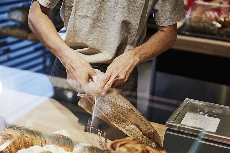 Person packt Backwaren in eine Brötchentüte. 