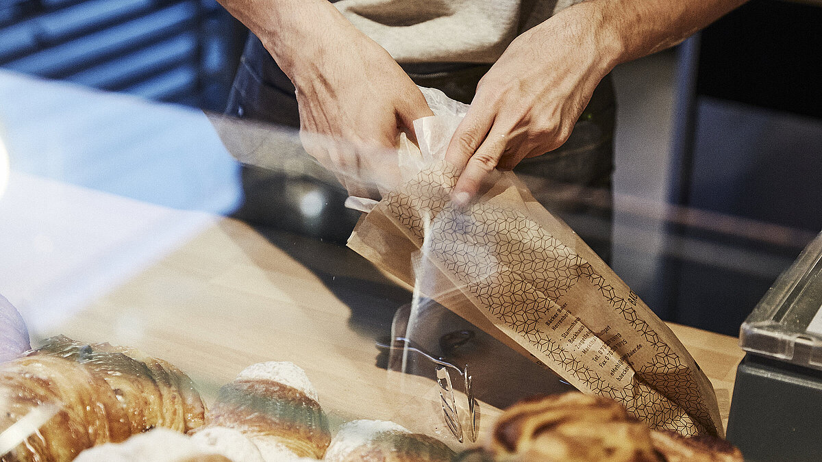 Person packt Backwaren in eine Brötchentüte. 