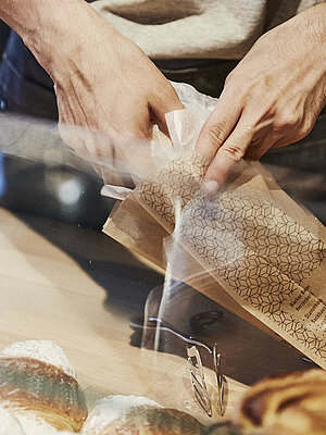 Person packt Backwaren in eine Brötchentüte. 