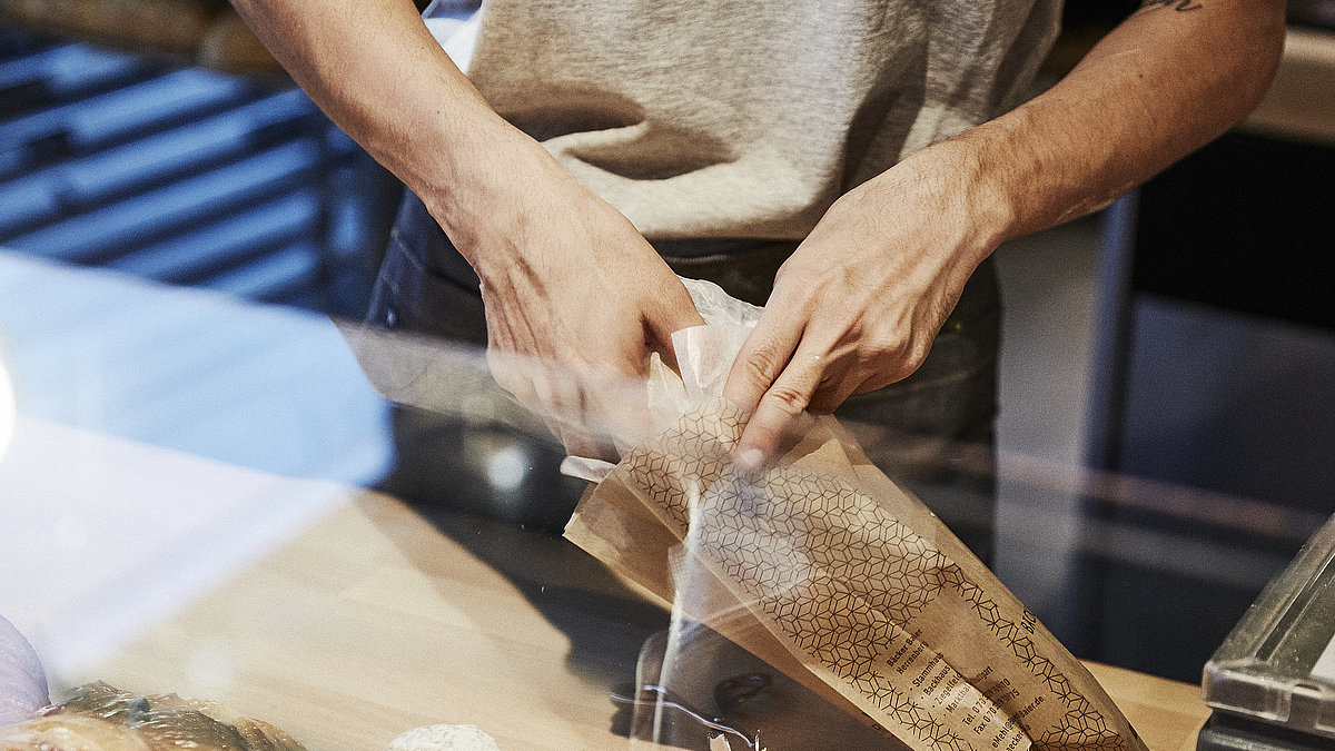 Person packt Backwaren in eine Brötchentüte. 