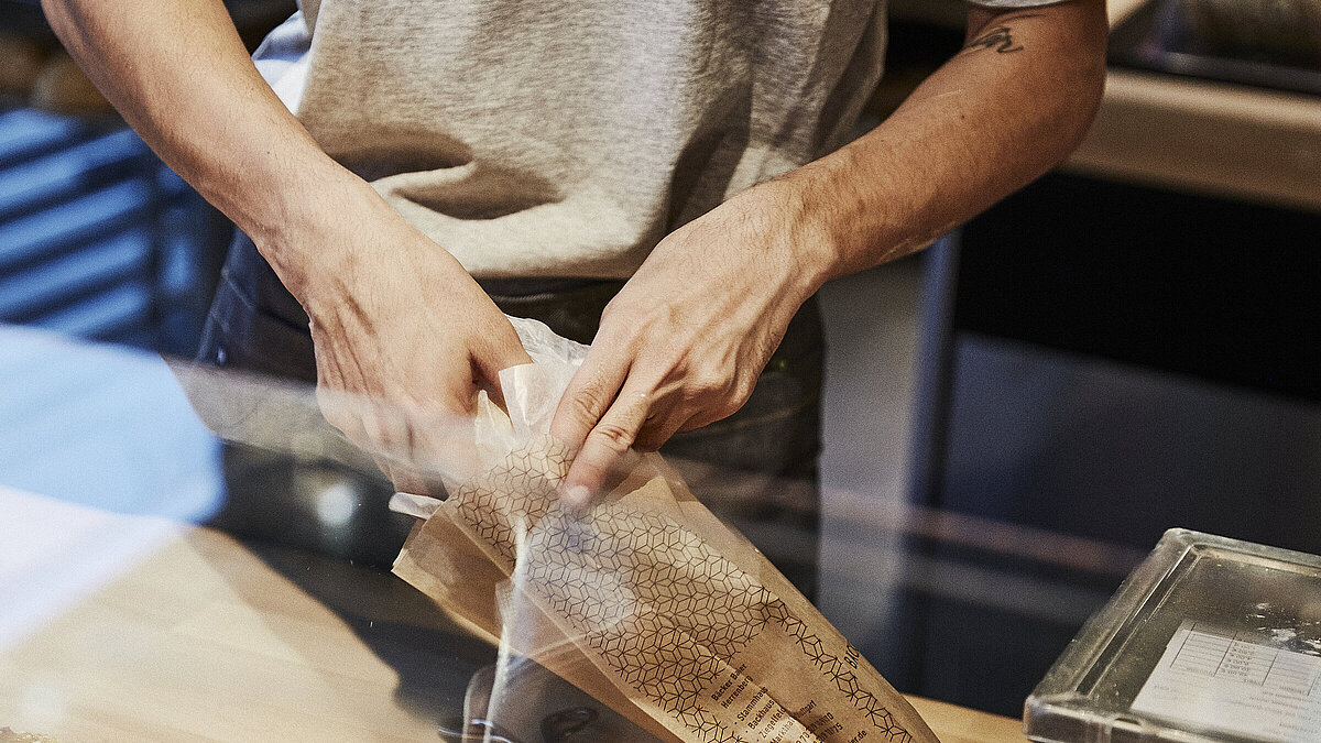 Person packt Backwaren in eine Brötchentüte. 