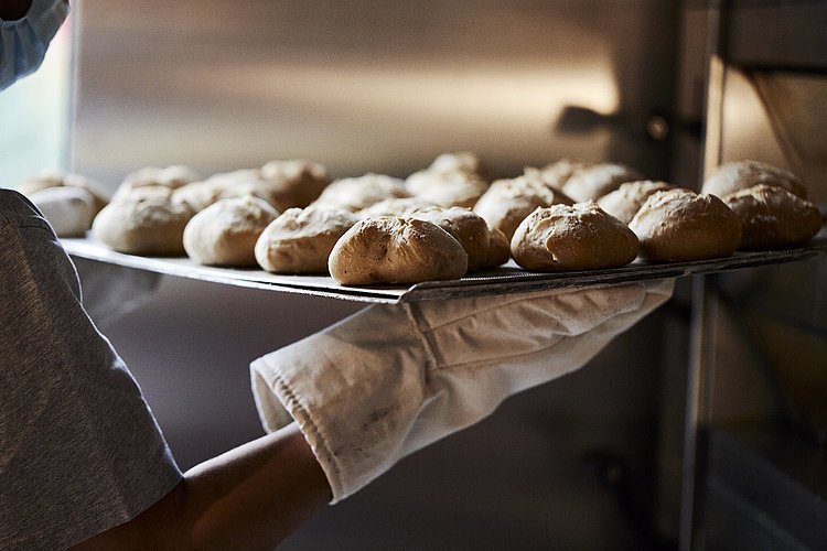 Ein Backblech mit frischen Brötchen wird aus dem Ofen geholt