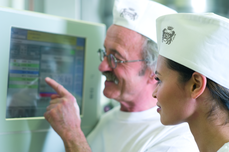 Bäckermeister und Bäckergesellin gucken in den Rezeptcomputer