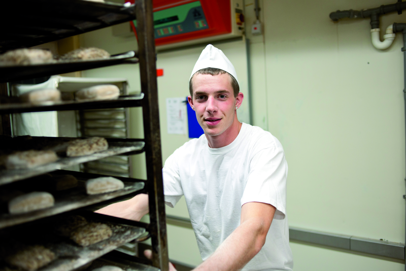 Bäckergeselle mit Brötchenteiglingen auf Stikken