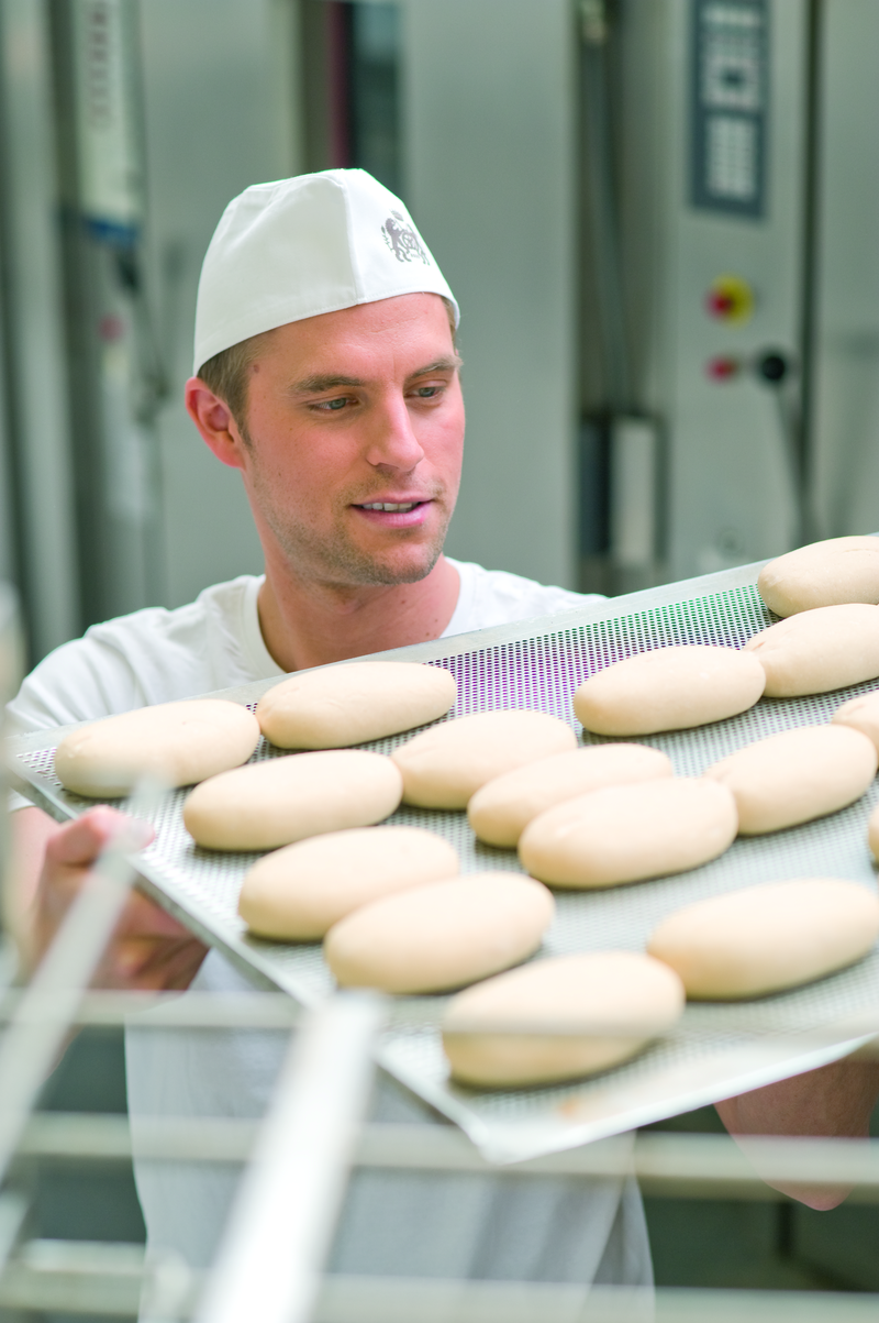Bäckergeselle trägt ein Backblech mit Brötchenteiglingen